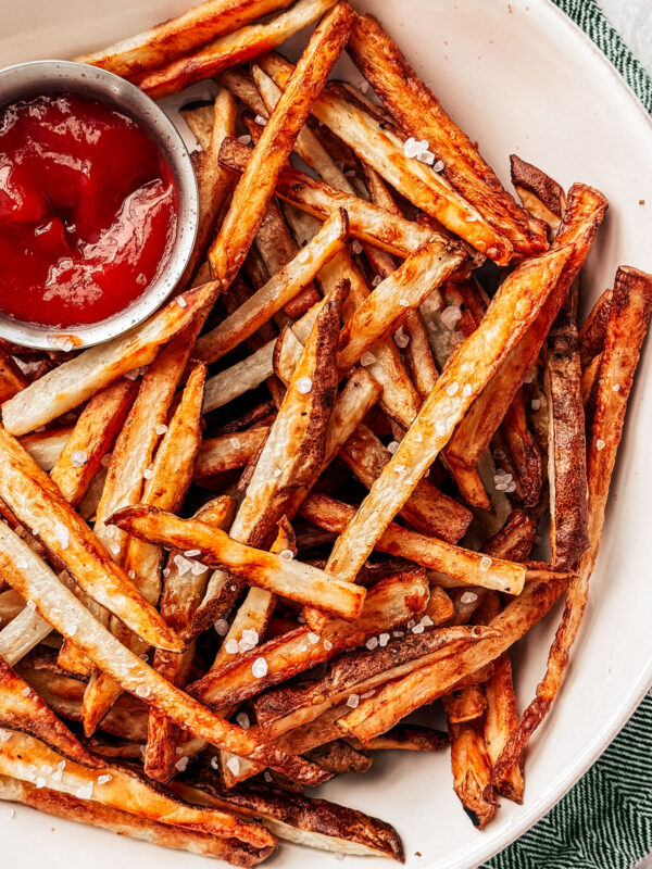 Air fryer french fries in a serving bowl with ketchup for dipping.