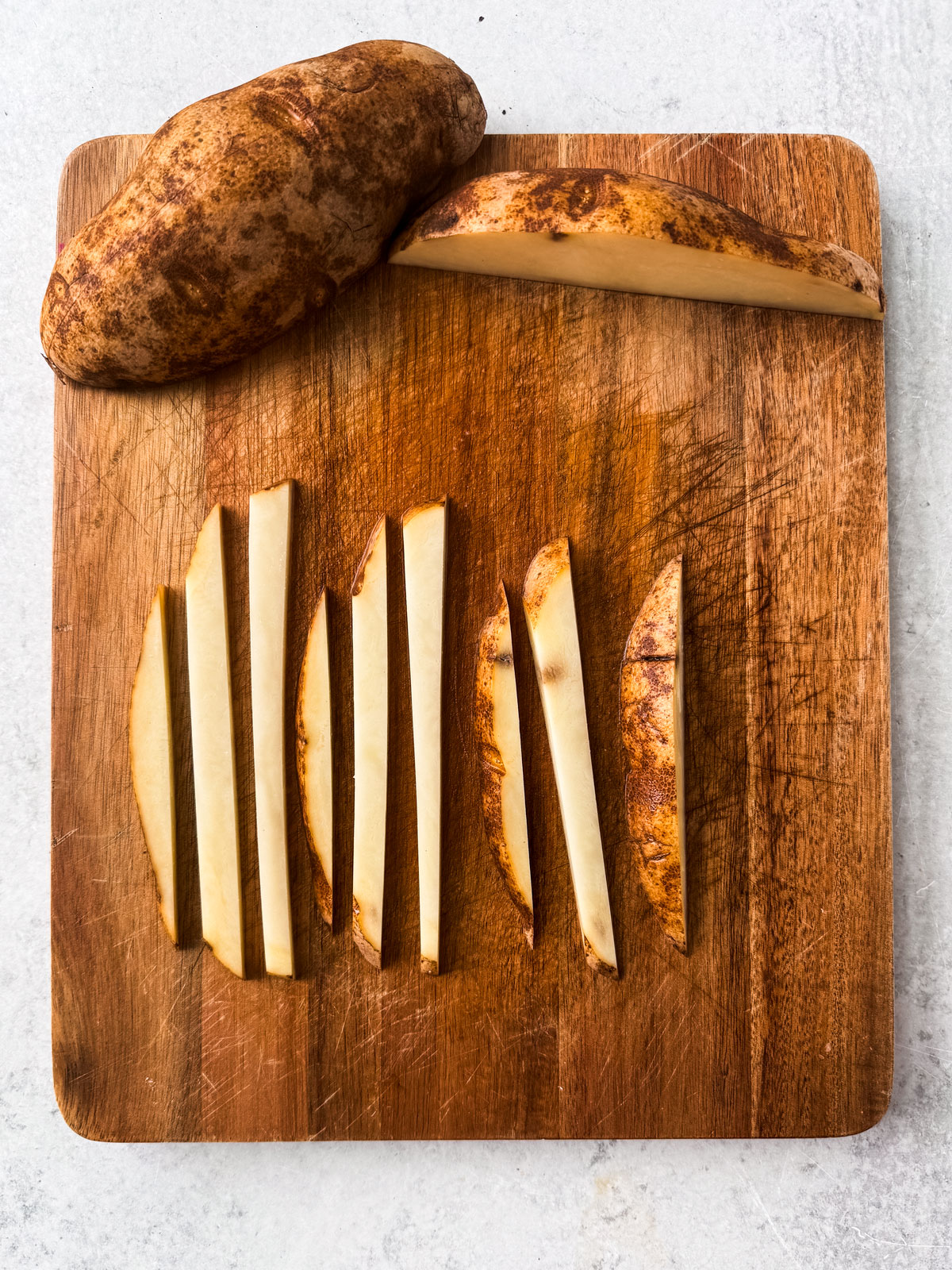 Uncooked fries cut up in uniform shapes on a cutting board.