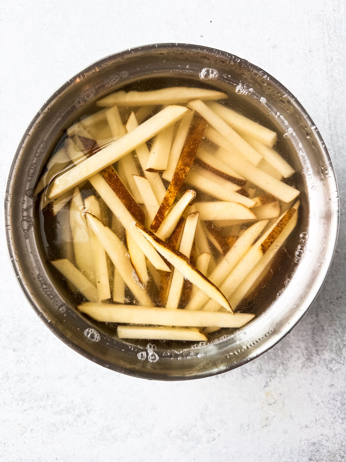 Uncooked fries soaking in a bowl of water.