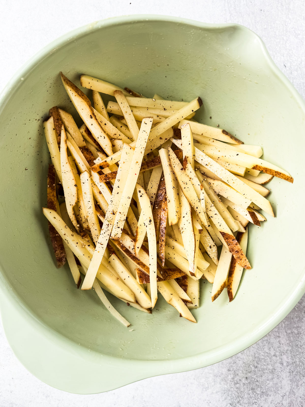 Uncooked fries in a mixing bowls with oil and seasoning.