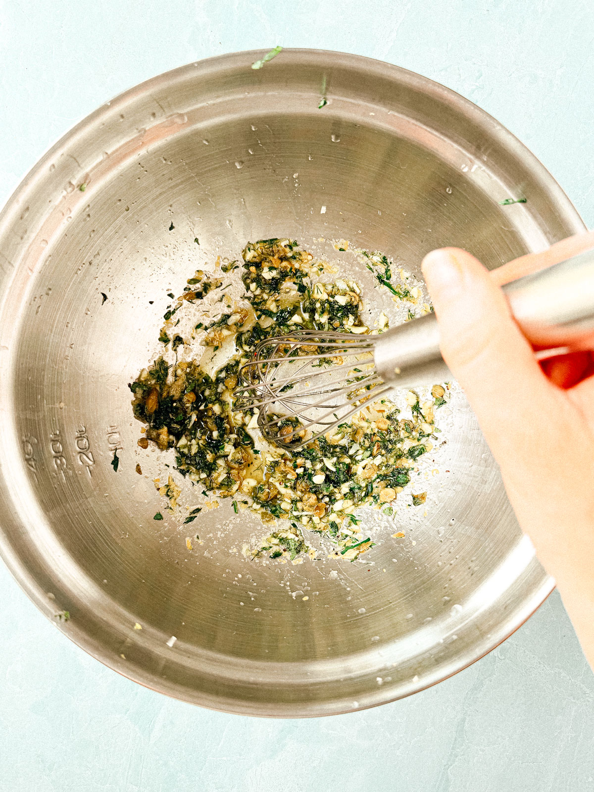 Mixing bowl with olive oil, garlic, and herbs being whisked. 