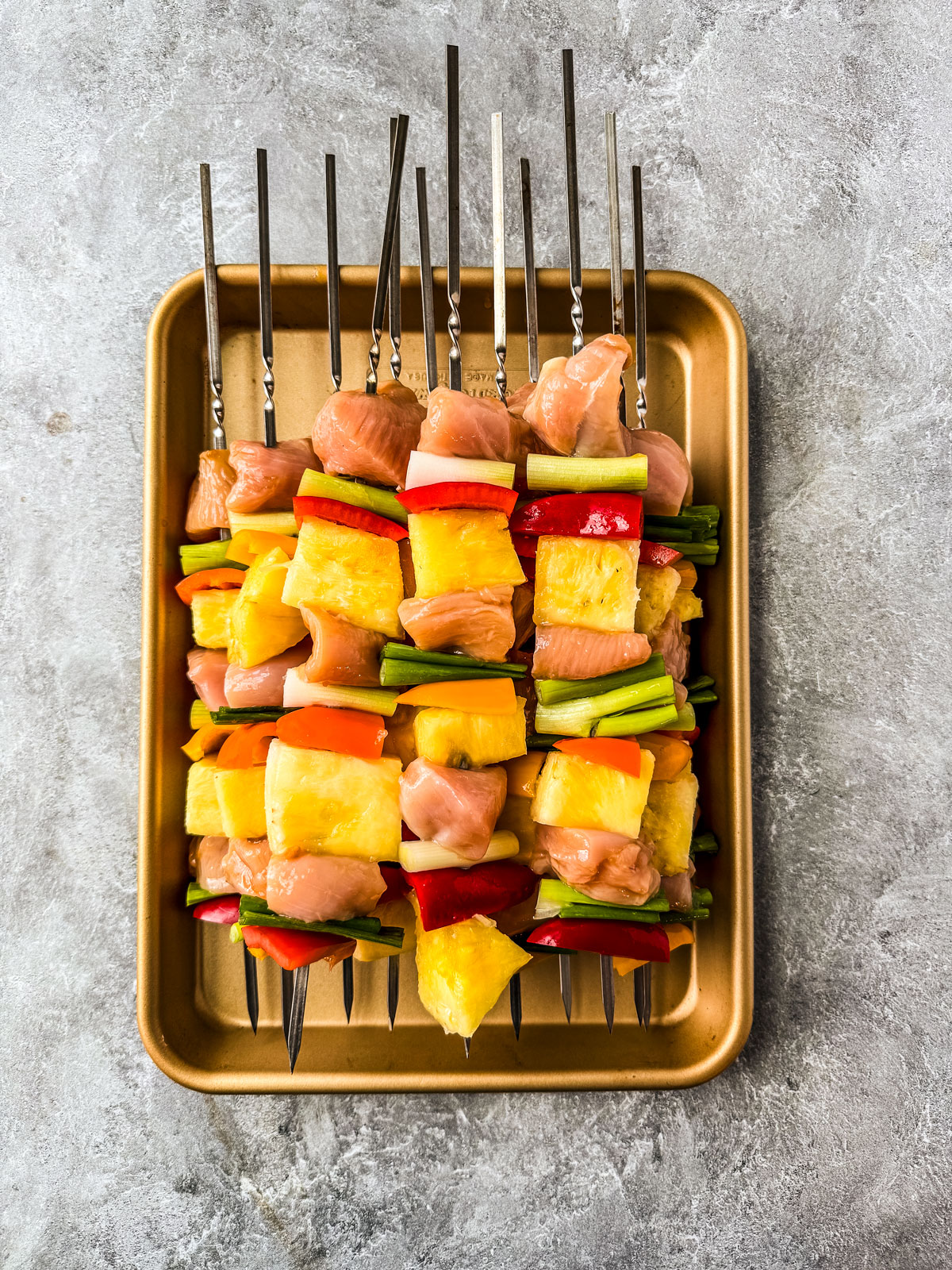 Uncooked pineapple chicken and veggies on skewers.