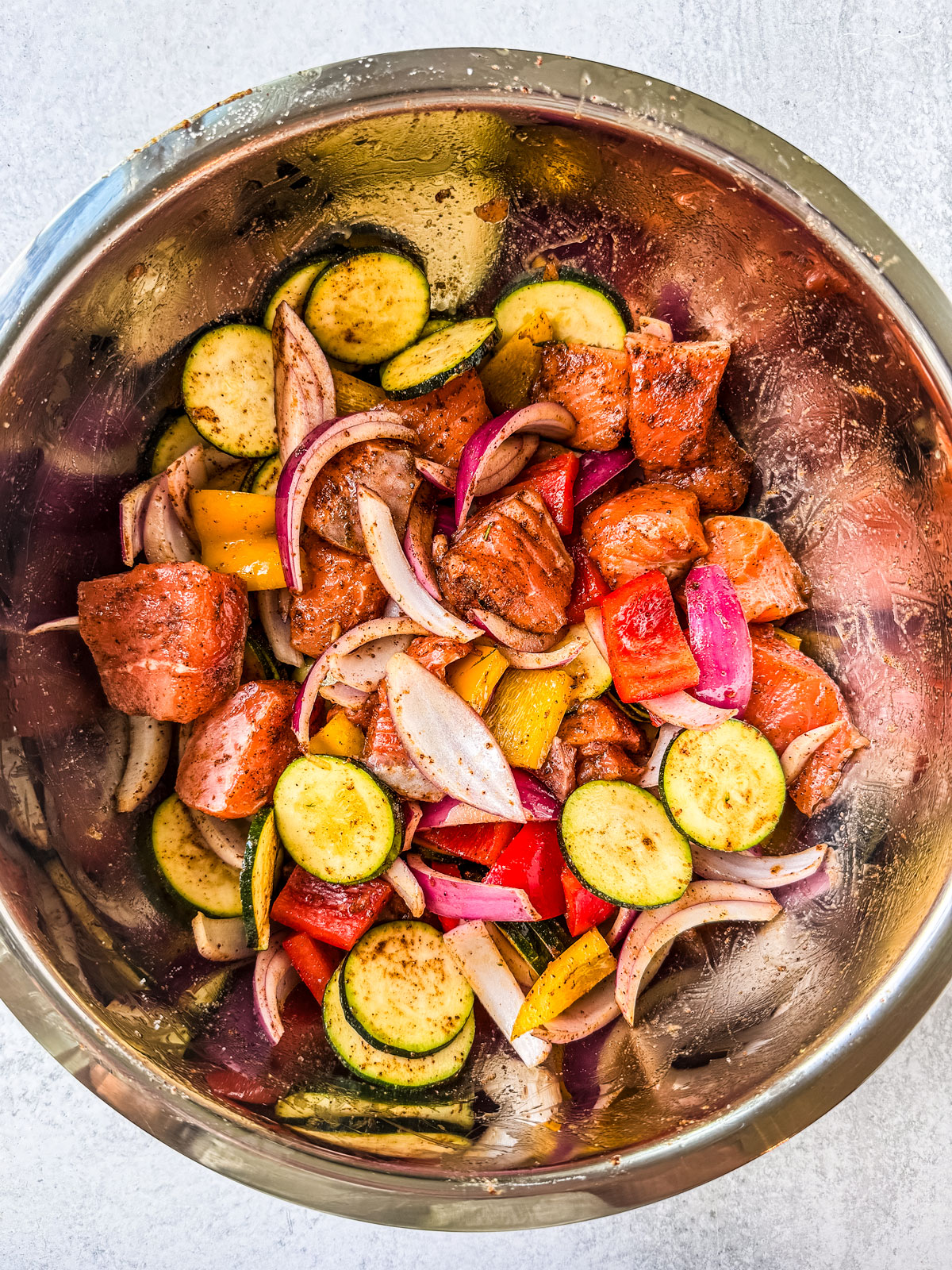 Salmon and vegetables tossed in marinade in a large mixing bowl.