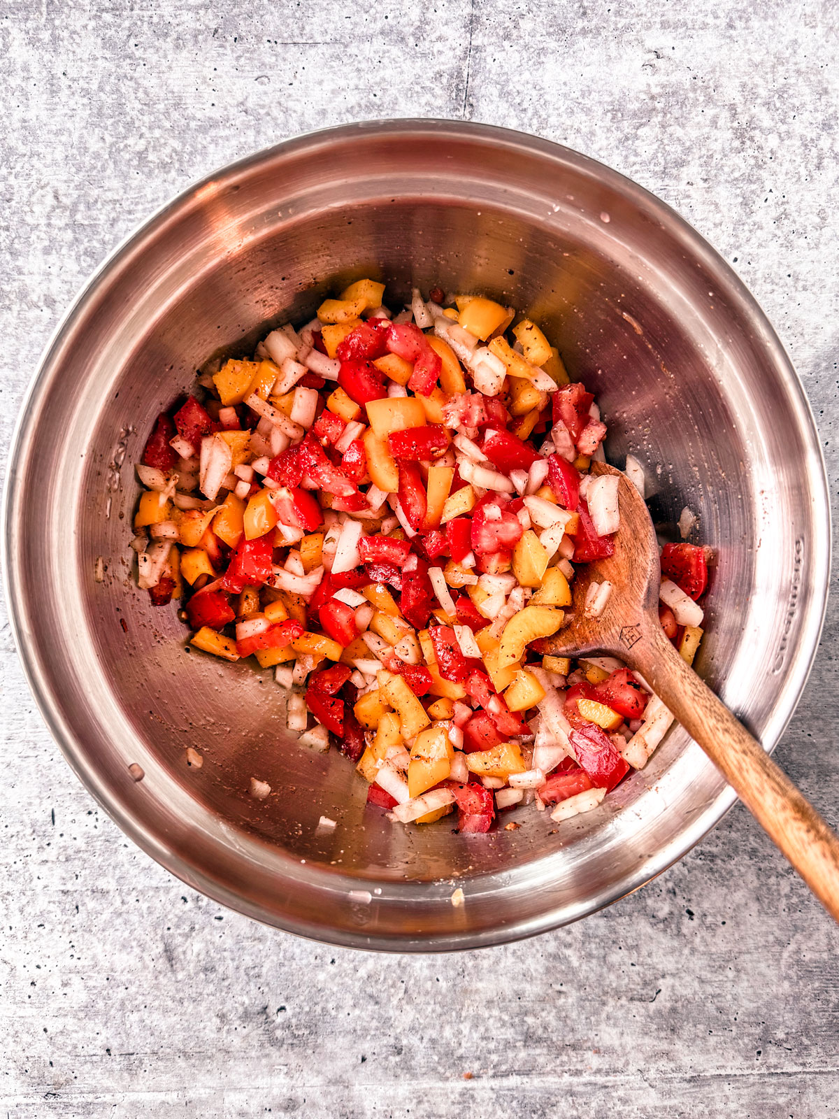 Tomatoes, onions, and bell pepper mixed in a mixing bowl.