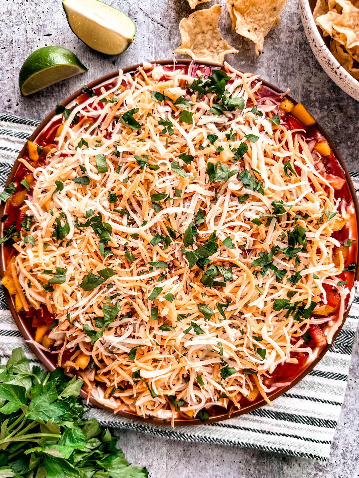 Taco dip with cream cheese on a serving plate next to a bowl of tortilla scoop chips.