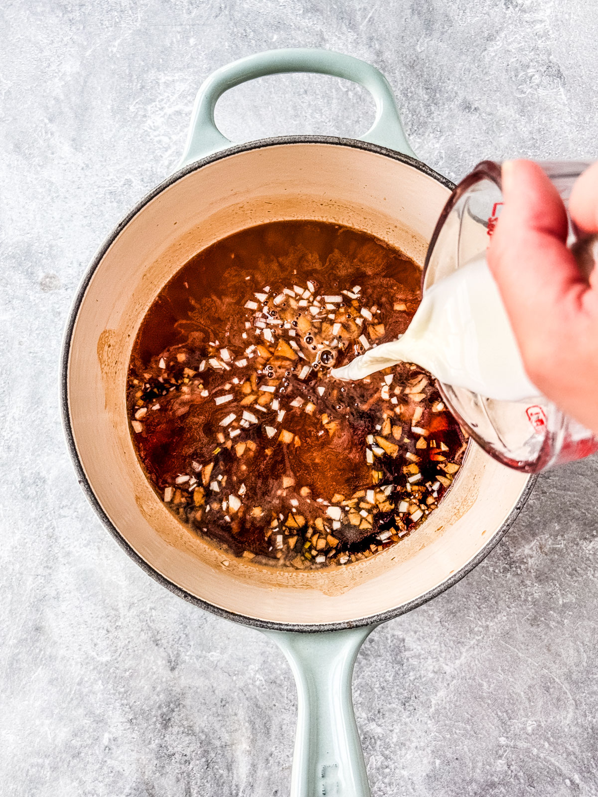 Slurry being poured into the sauce in the saucepan.