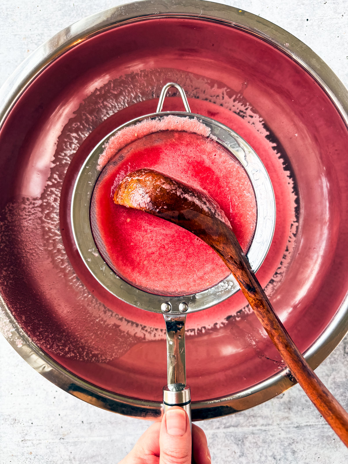 Puréed watermelon being trained through a sieve into a large mixing bowl.