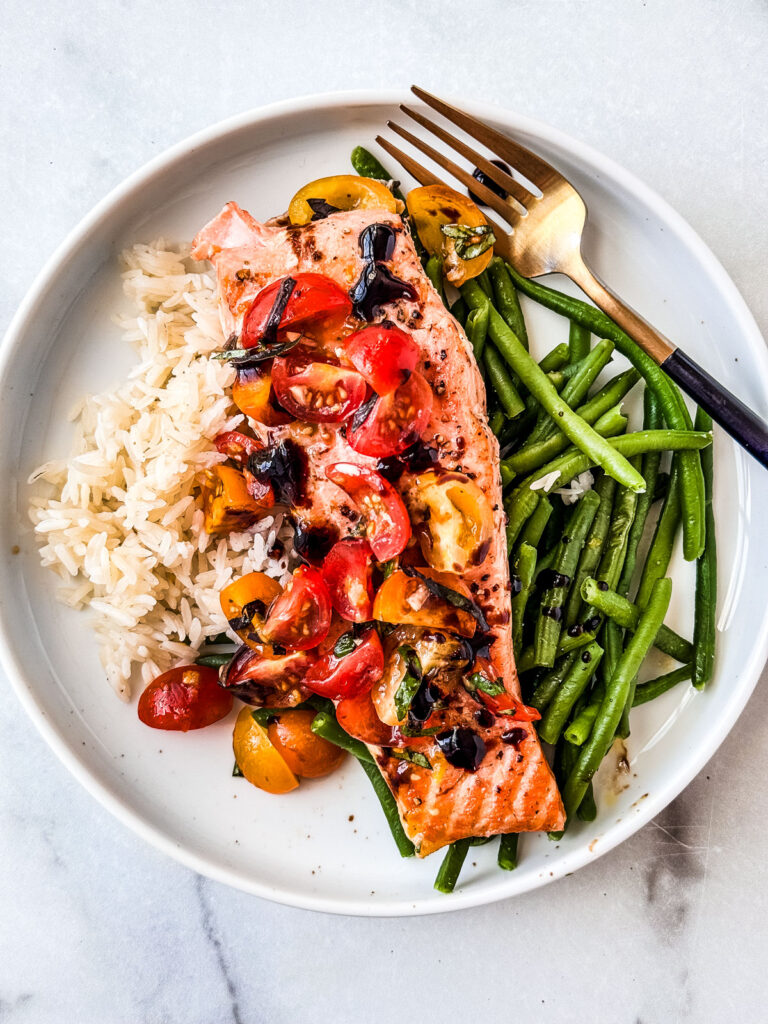 Fillet of salmon with bruschetta topping on a plate with rice and green beans.