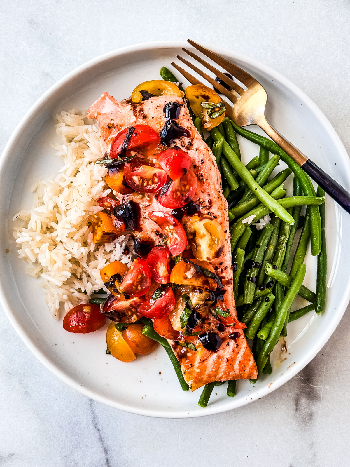 Grilled salmon with cherry tomato bruschetta topping on a plate with rice and green beans.