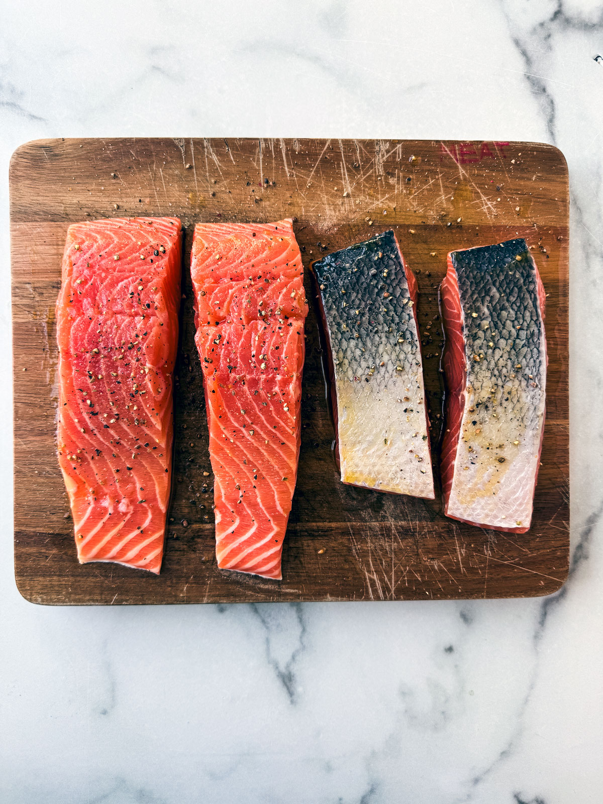 Fillets of salmon seasoned and oiled on a wooden cutting board.