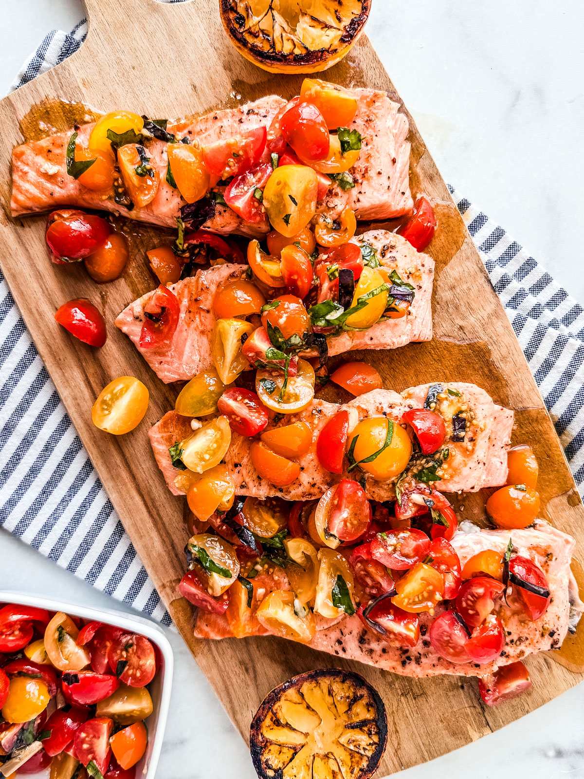 Grilled salmon topped with cherry tomato bruschetta on a serving board.
