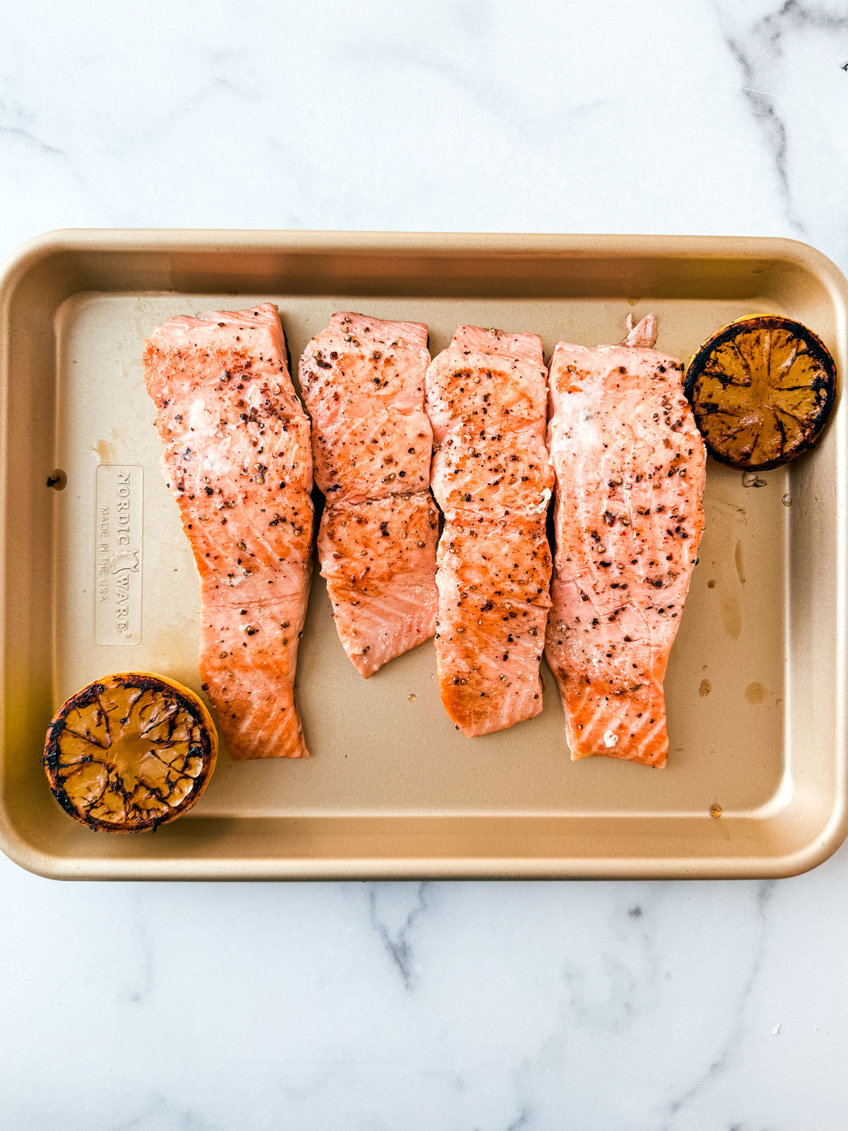 Cooked fillets of salmon on a small baking sheet with charred grilled lemon halves.