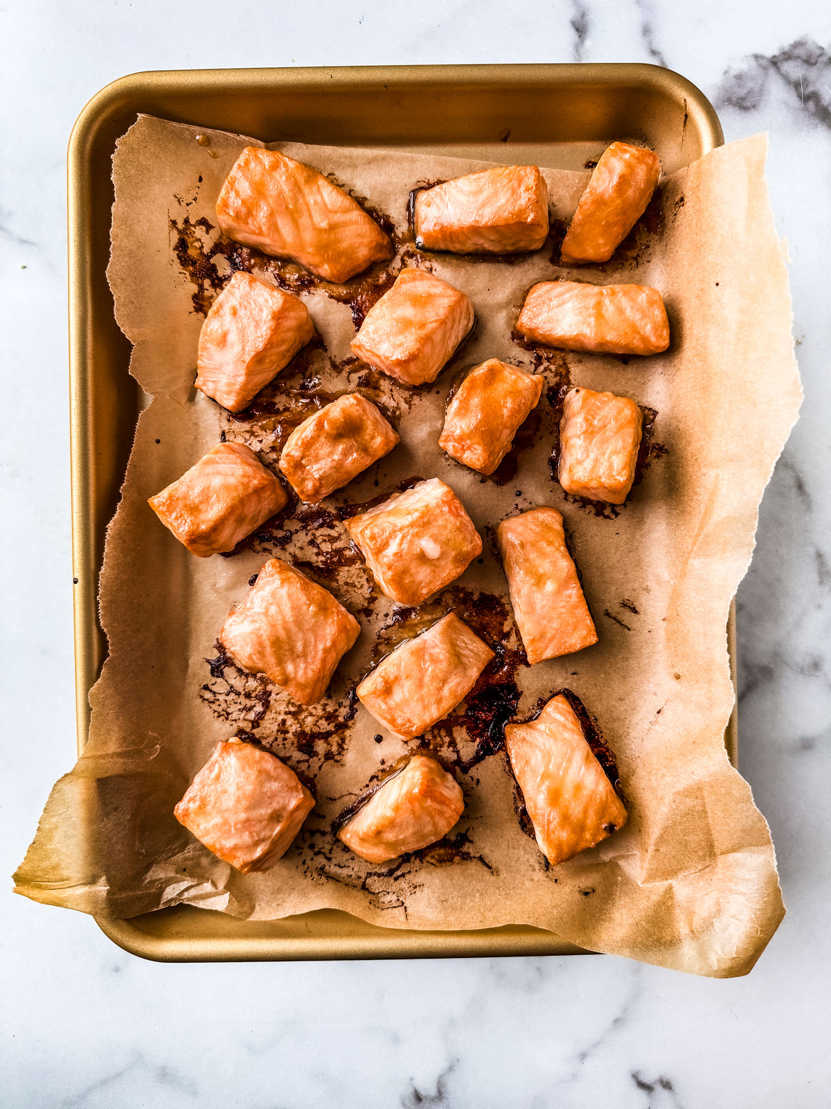 Cooked salmon cubes on a parchment-lined baking sheet.