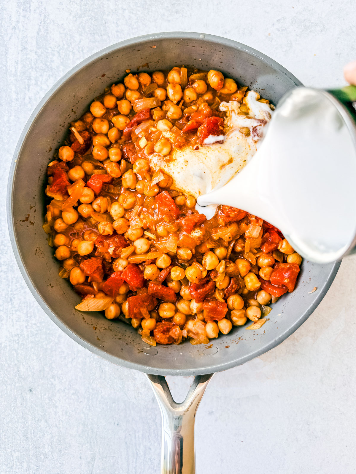 Coconut milk being poured into the skillet with the chickpeas and tomatoes.