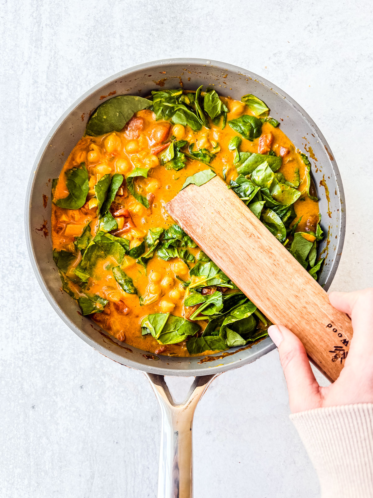 Spinach being stirred into the chickpea curry with coconut milk.