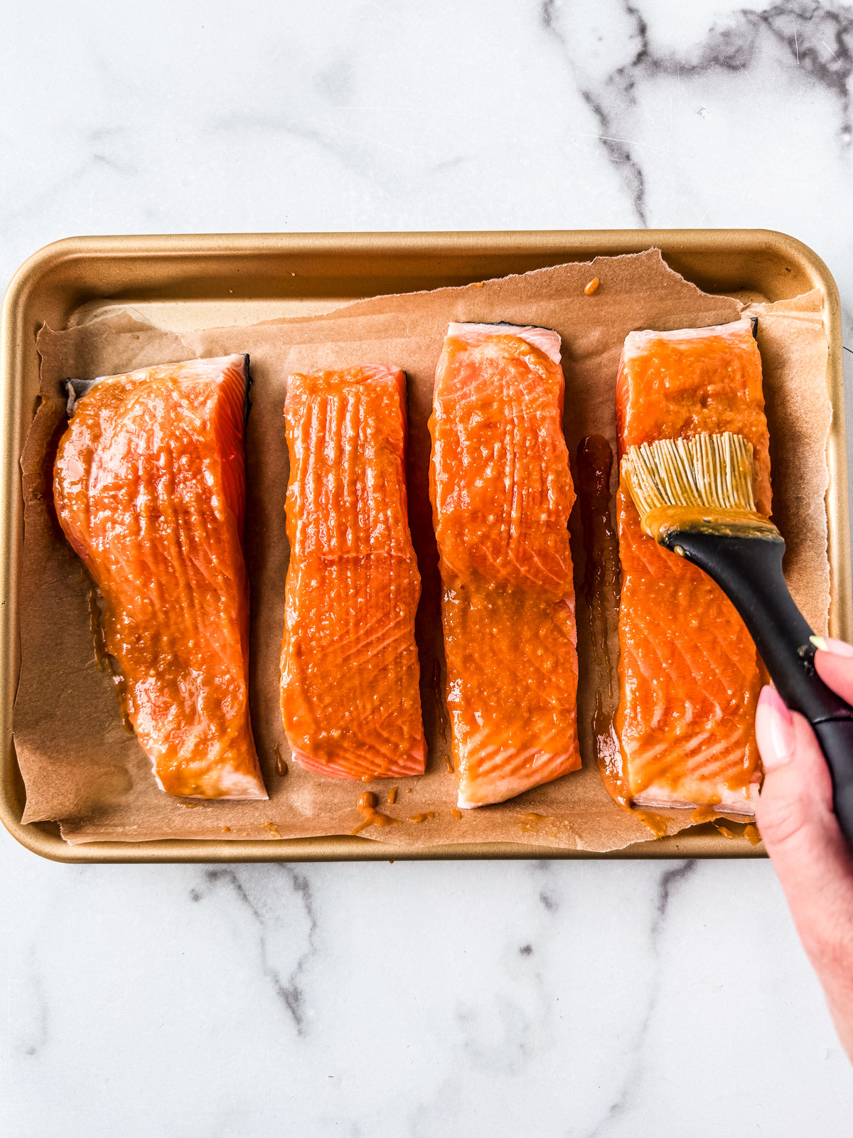 Hand brushing miso sauce over fillets.