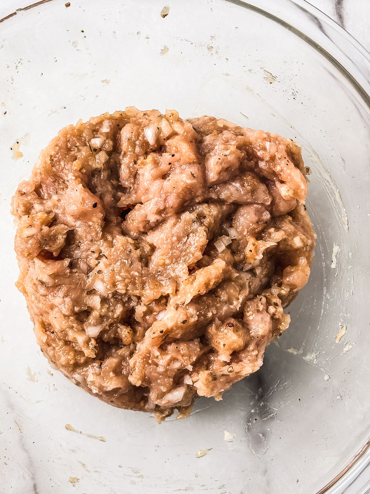 Ground chicken meatball mixture in a glass bowl.