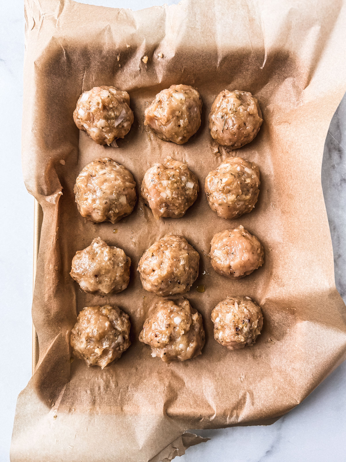 Ground chicken meatballs formed and set on parchment-covered baking sheet.