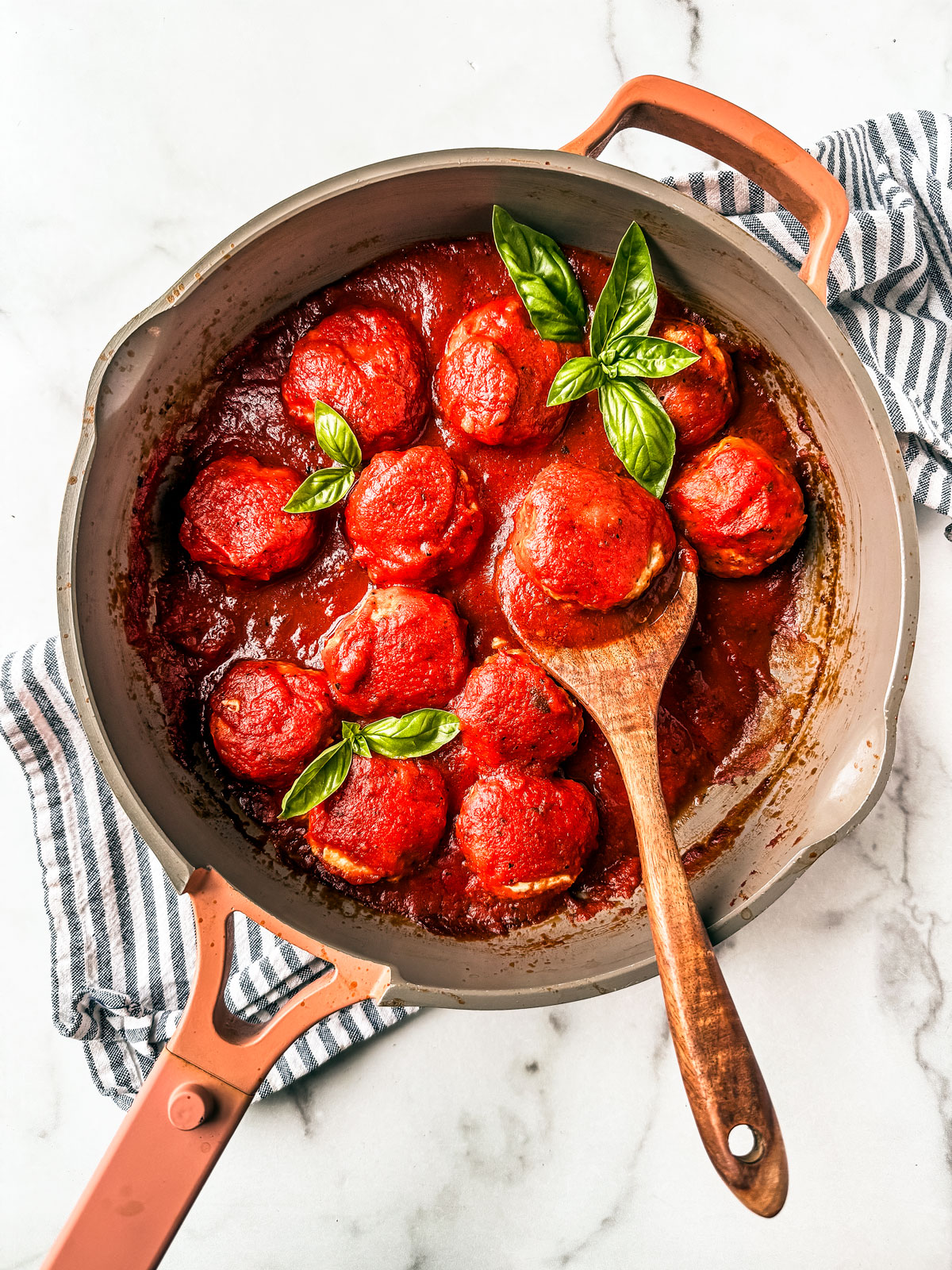 Saucepan full of ground chicken meatballs in marinara sauce with basil leaves and a wooden spoon.