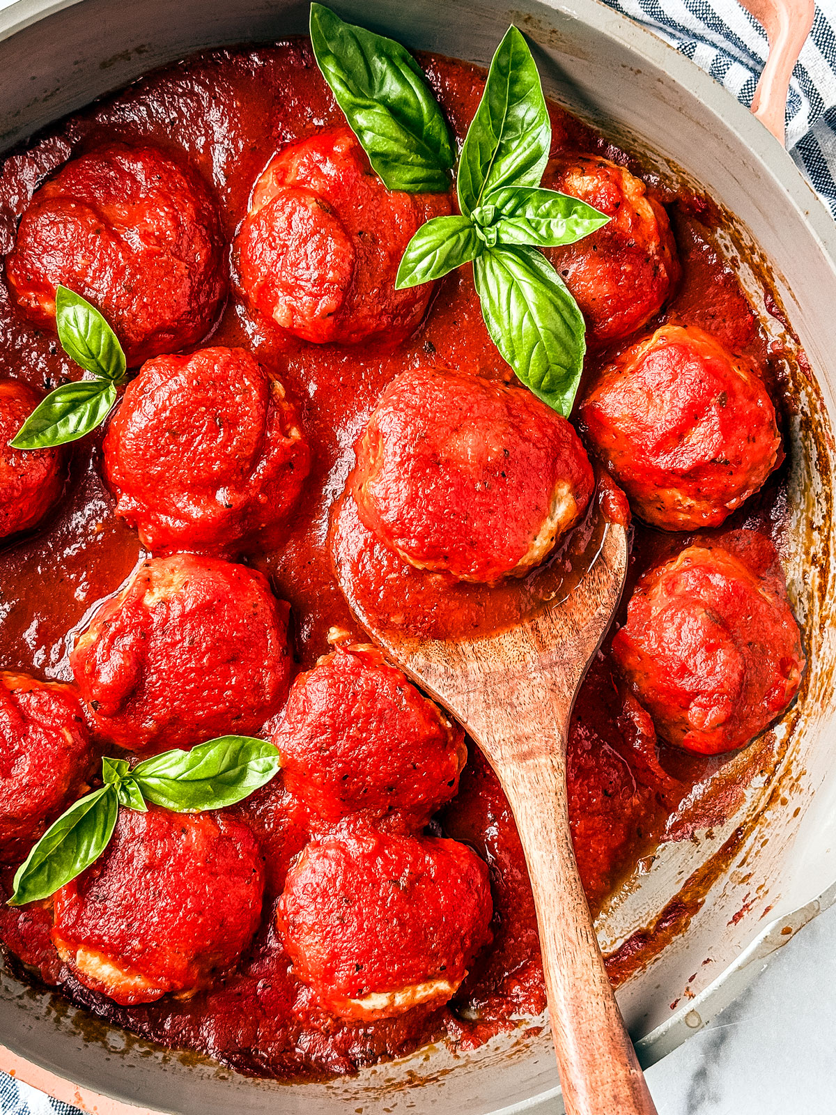 Saucepan with chicken meatballs in marinara sauce and fresh basil leaves.