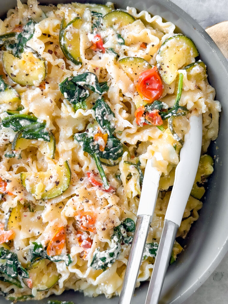 Pan with creamy noodles tossed with zucchini, tomatoes, and spinach.