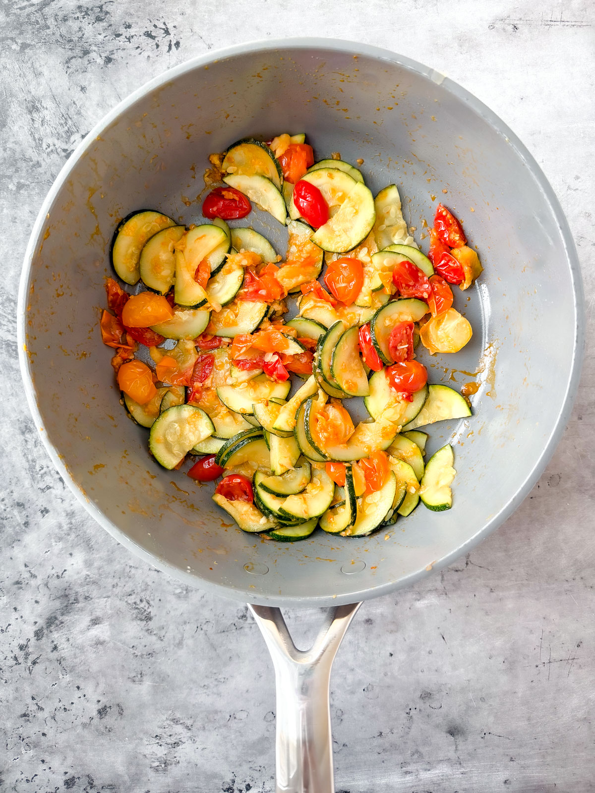 Zucchini and tomatoes being sautéed in a pan.