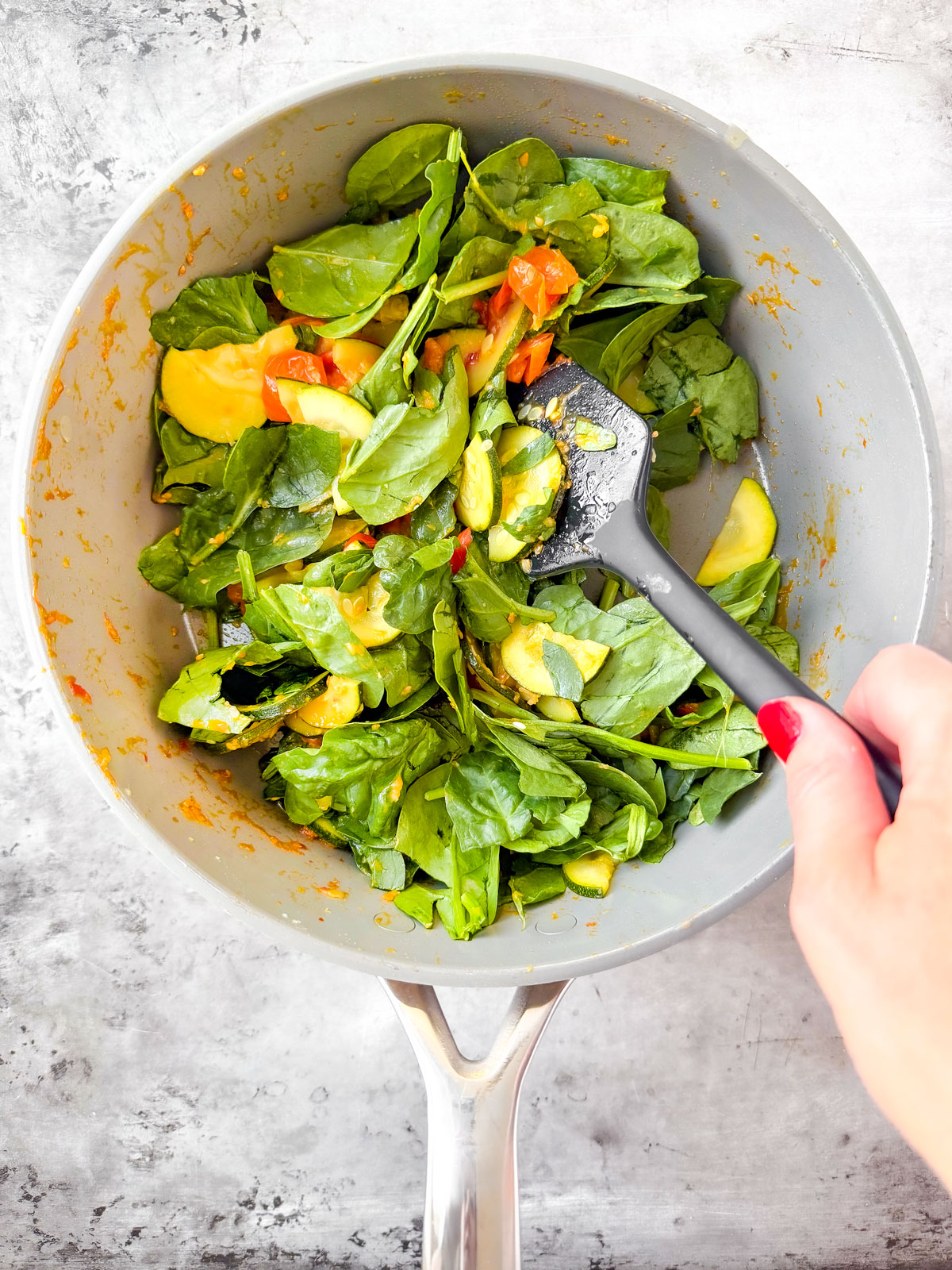 Sauté pan with veggies and spinach added, being stirred.