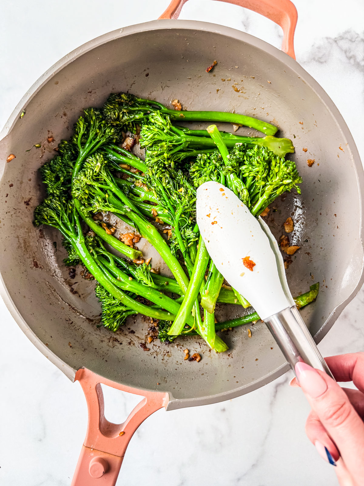 Bright green cooked broccolini being tossed in garlic and ginger.