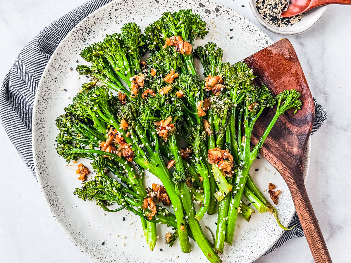 Serving plate of sauteed broccolini with a wooden spatula.