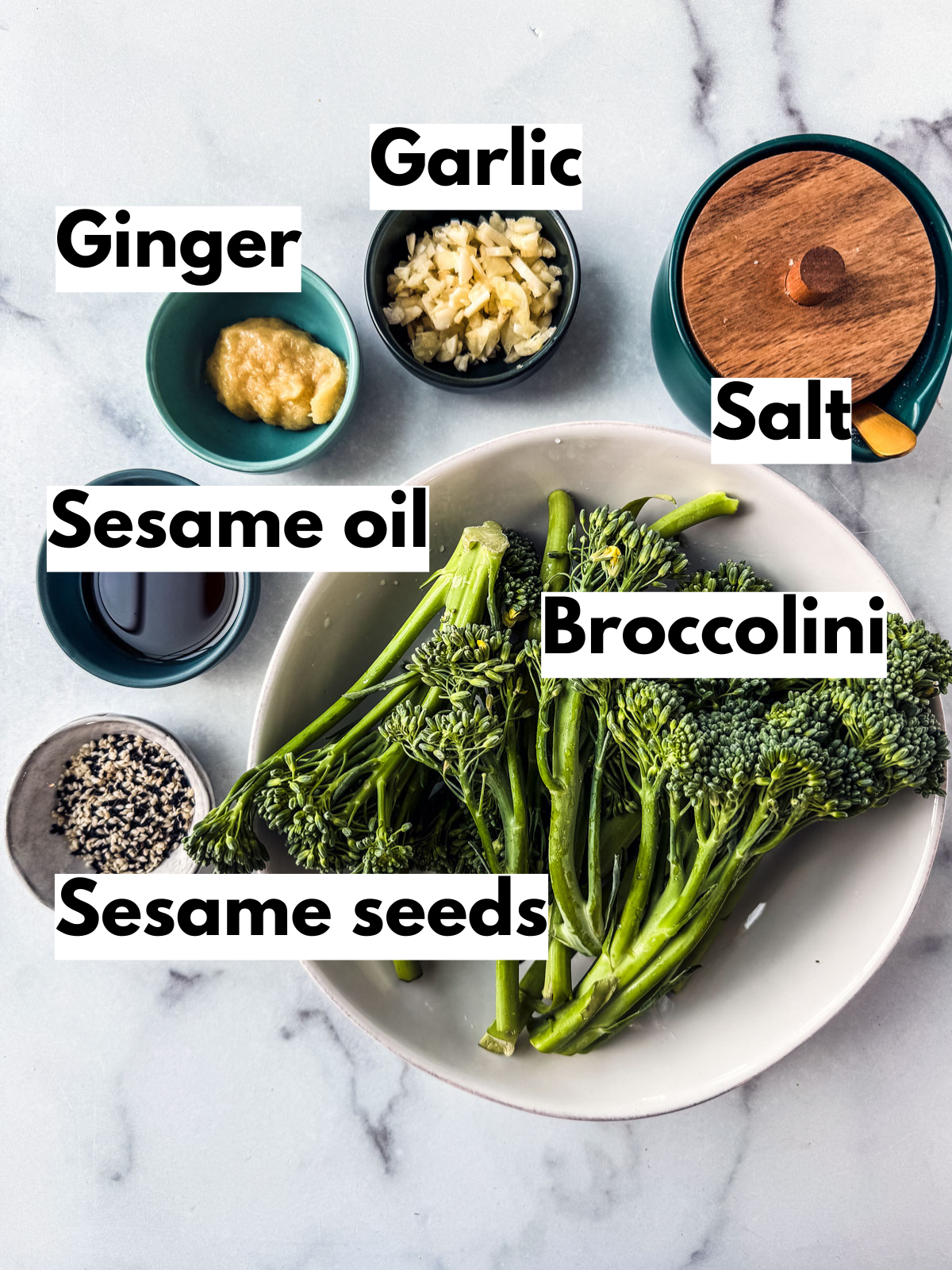 Ingredients for garlic ginger sautéed broccolini spread out over a white marble background. 