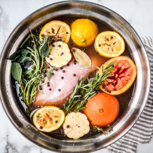 Large mixing bowl full of turkey brine and a turkey breast.