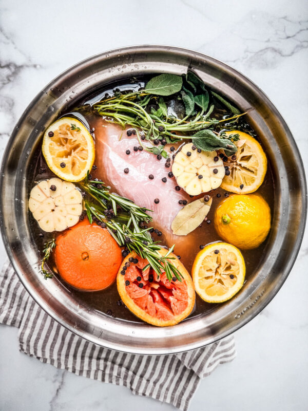 Large mixing bowl full of apple cider turkey brine, citrus fruit, herbs, and turkey breast.