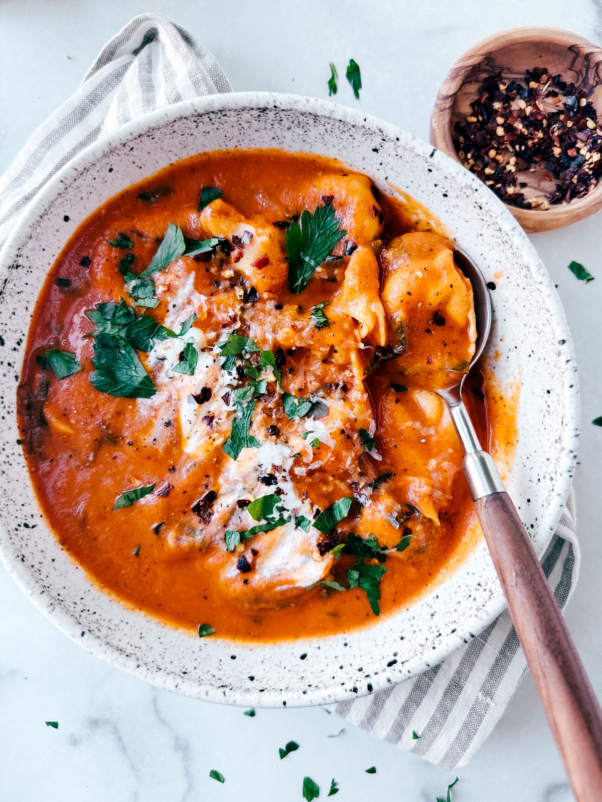 Bowl of tomato tortellini soup garnished with cheese and parsley.