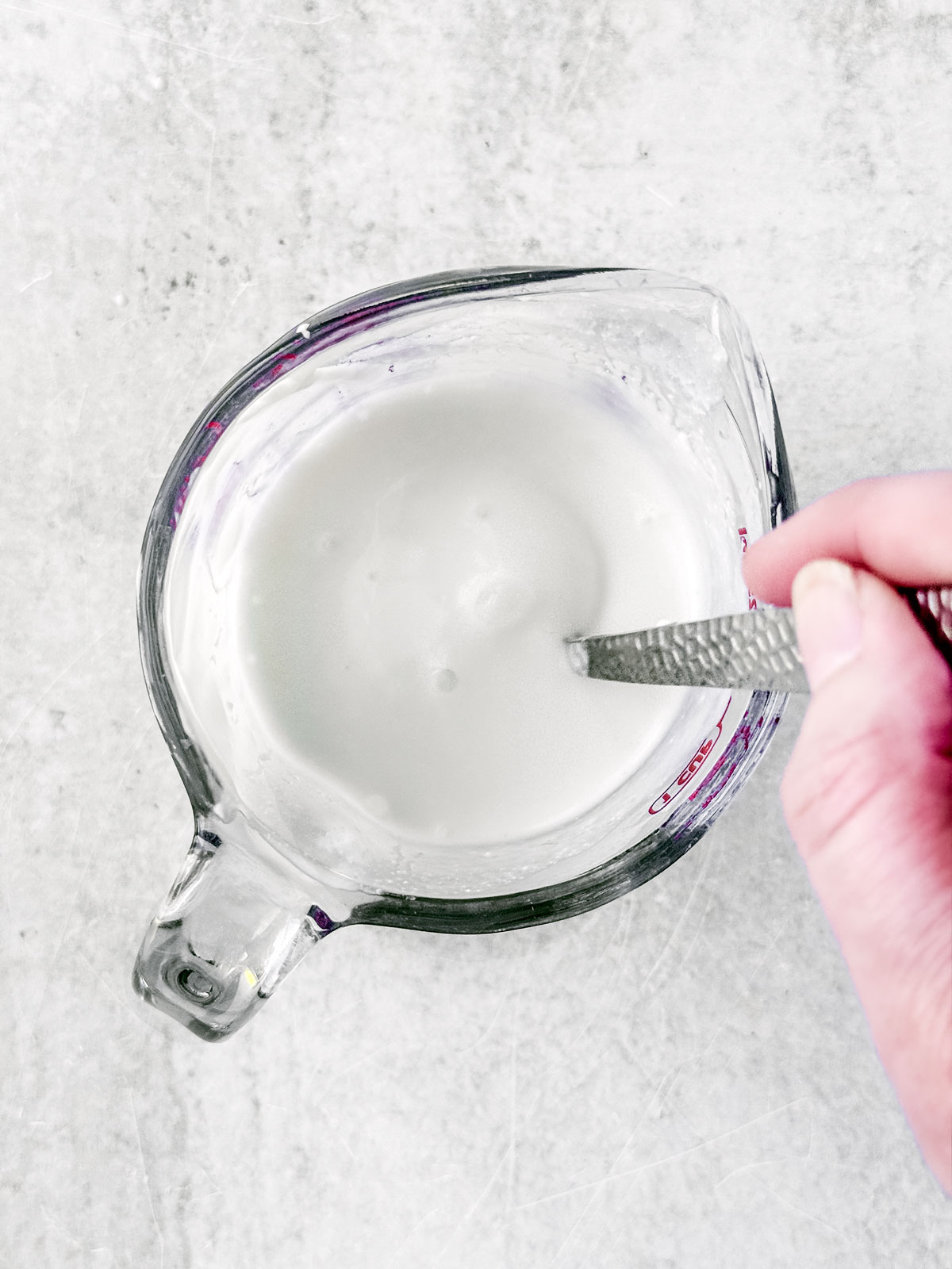 Greek yogurt being mixed with water in a measuring cup.