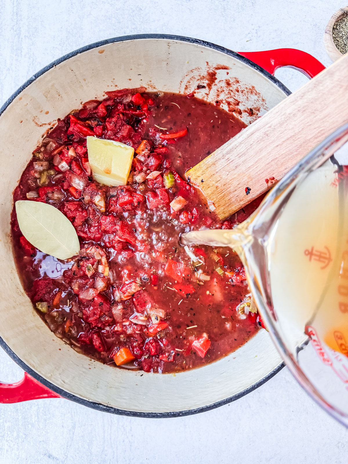 Pot of veggies and tomatoes with broth being added.