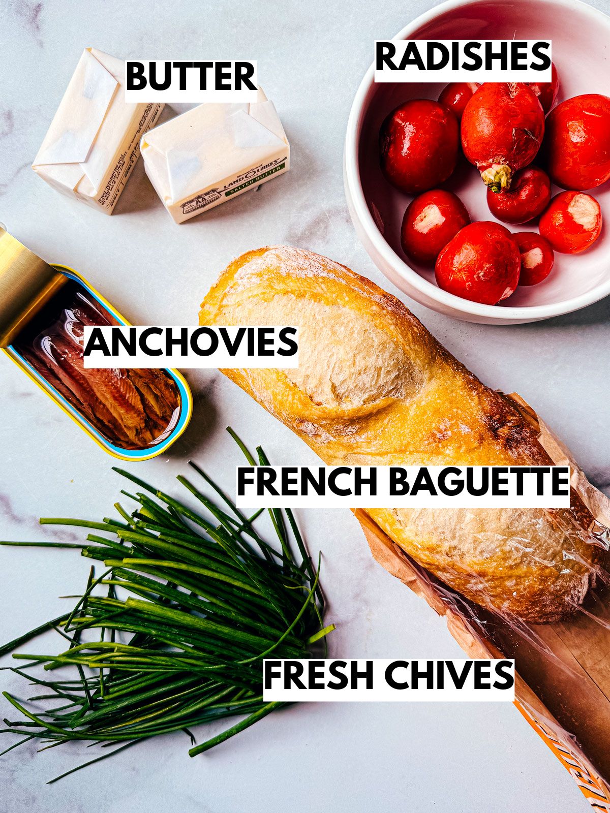 Ingredients for radish and anchovy butter on baguette slices on a white background.