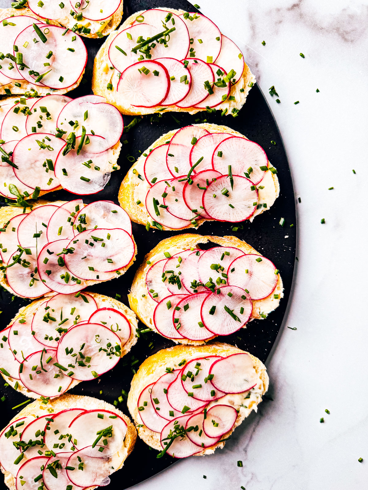 Anchovy butter on baguette slices with radishes spread out on a serving board.