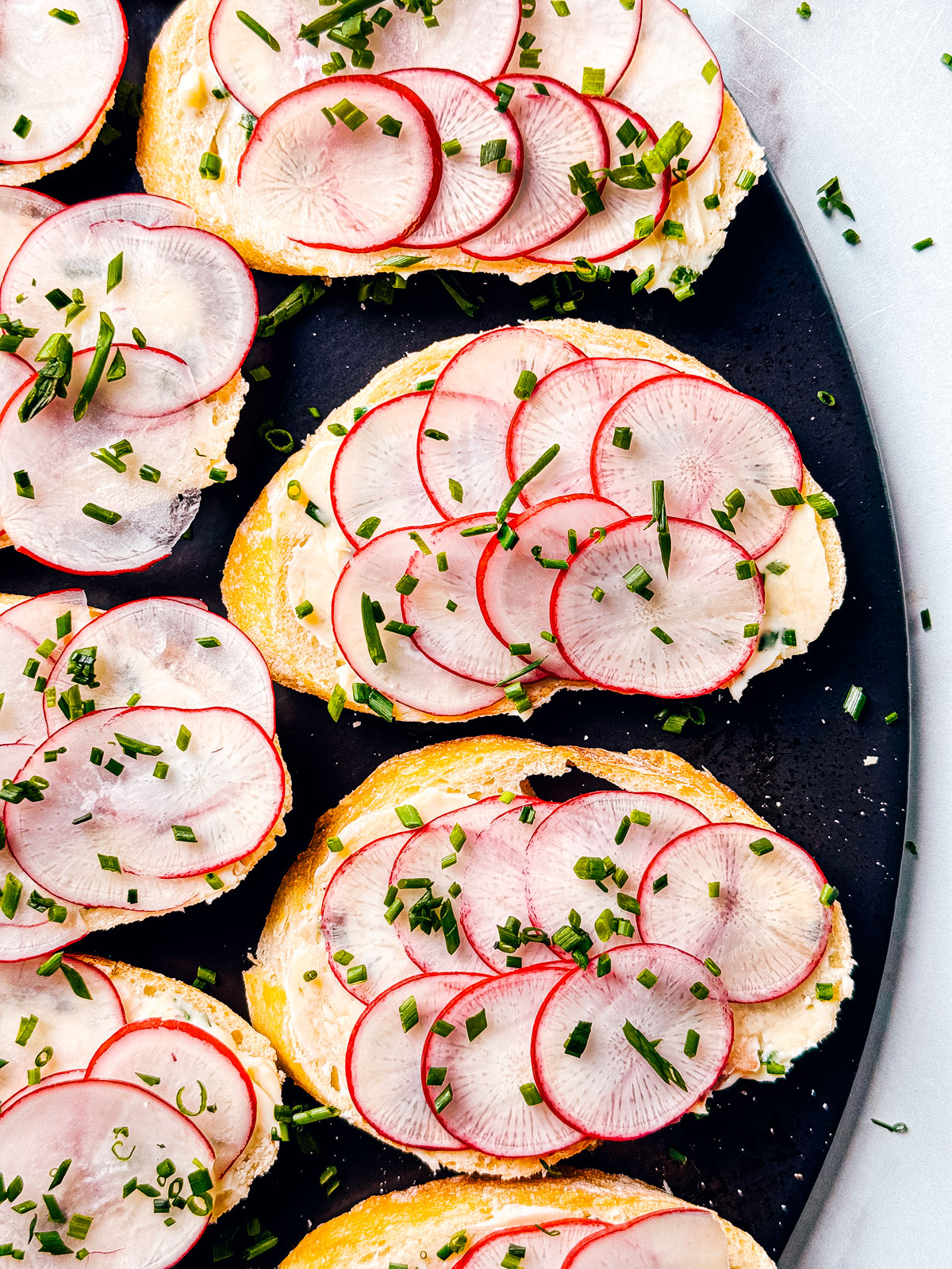 Anchovy butter on baguette slices with radishes spread out on a serving board.