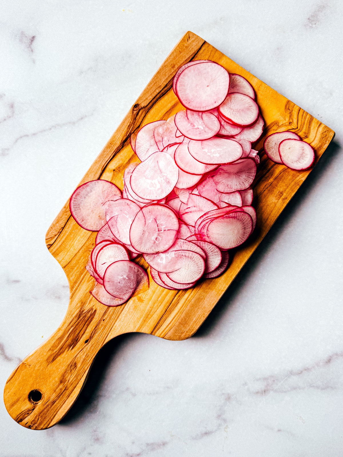 Thinly sliced radishes on a small cutting board.