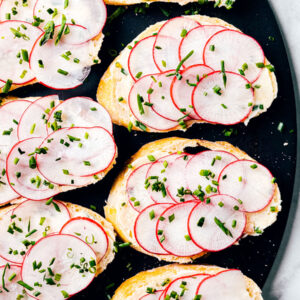 Baguette slices with anchovy butter and radishes on a serving platter.