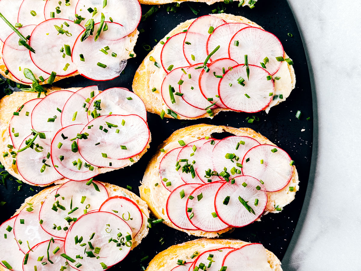 Anchovy butter on baguette slices with radishes spread out on a serving board.