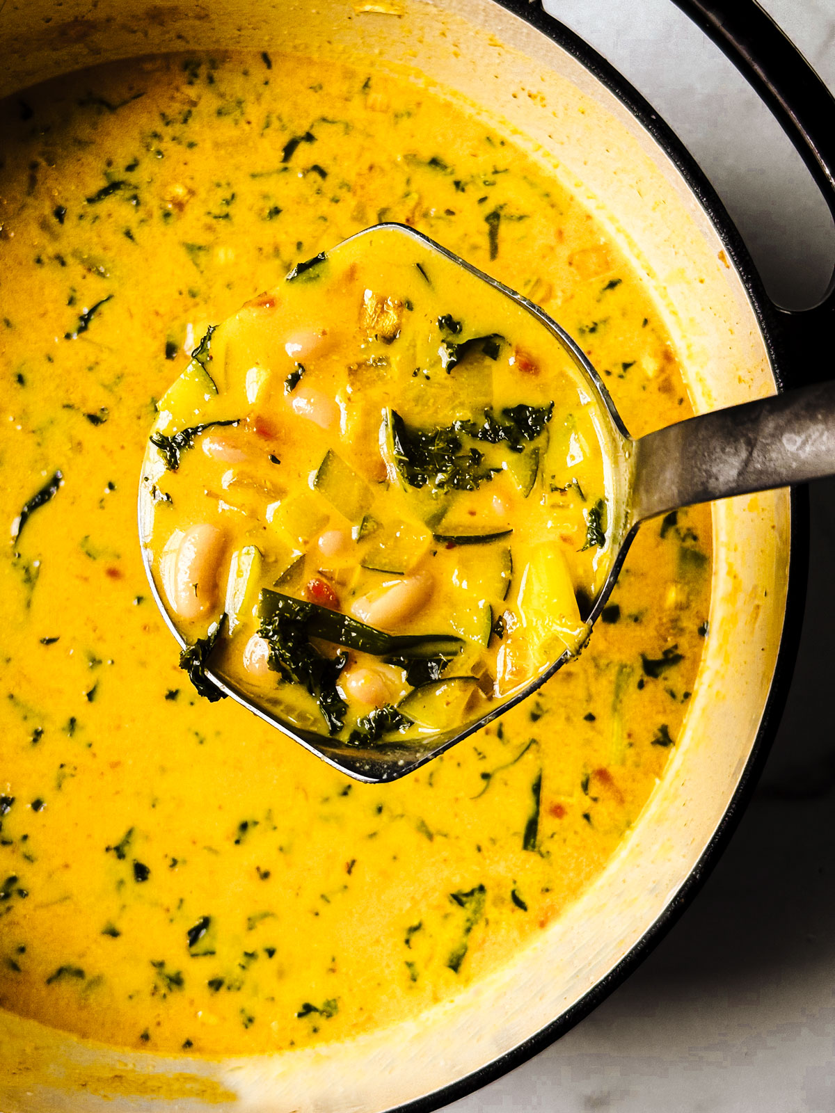 Kale and white bean Thai curry soup being ladled upward toward the camera.