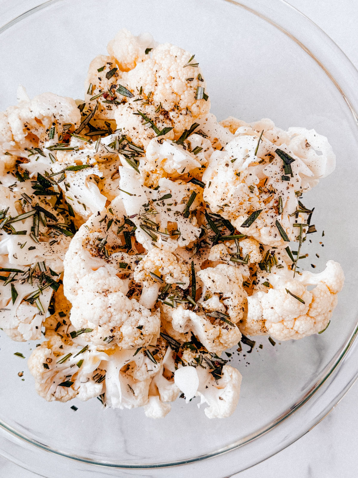 Cauliflower and onions tossed in olive oil and rosemary in a glass bowl.