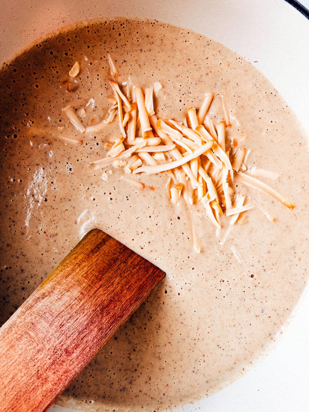 Soup in a pot with shredded cheese being stirred into it.