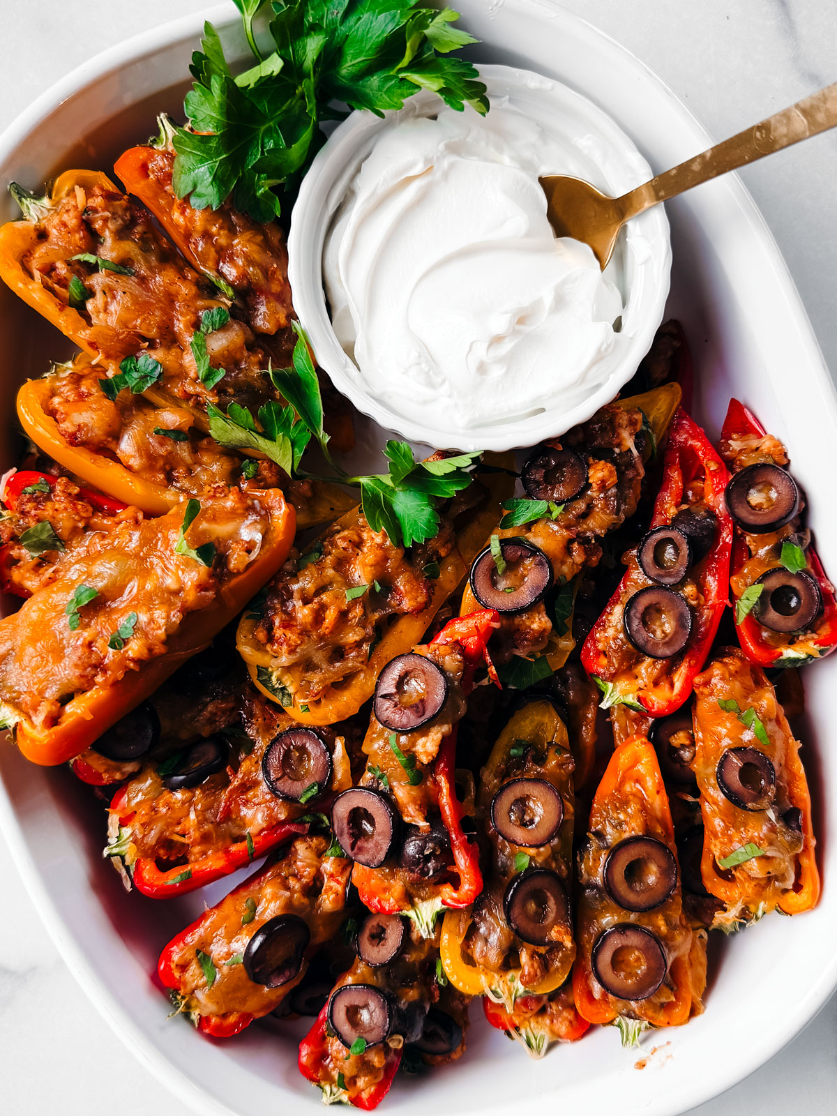 White baking dish with taco stuffed mini peppers served with bowl of sour cream.