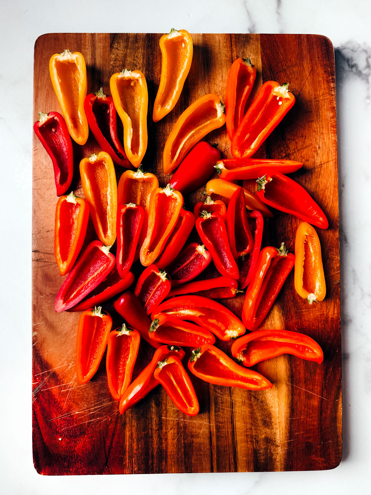 Cutting board with washed and gutted mini peppers halves.