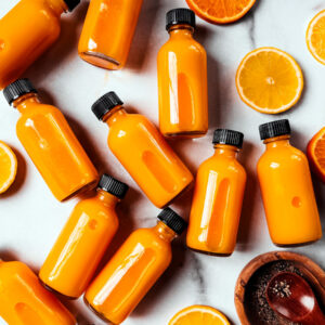 Turmeric ginger shots on a marble background with lemon and orange slices.