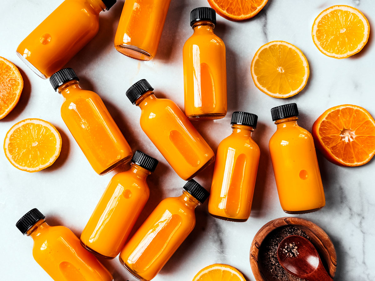 Turmeric ginger shots spread out over a white marble background with lemon and orange slices.