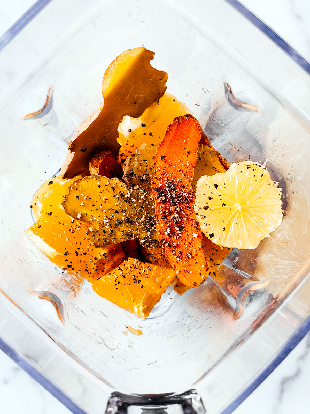 Orange and lemon segments in a blender with ginger root, turmeric root, and pepper.