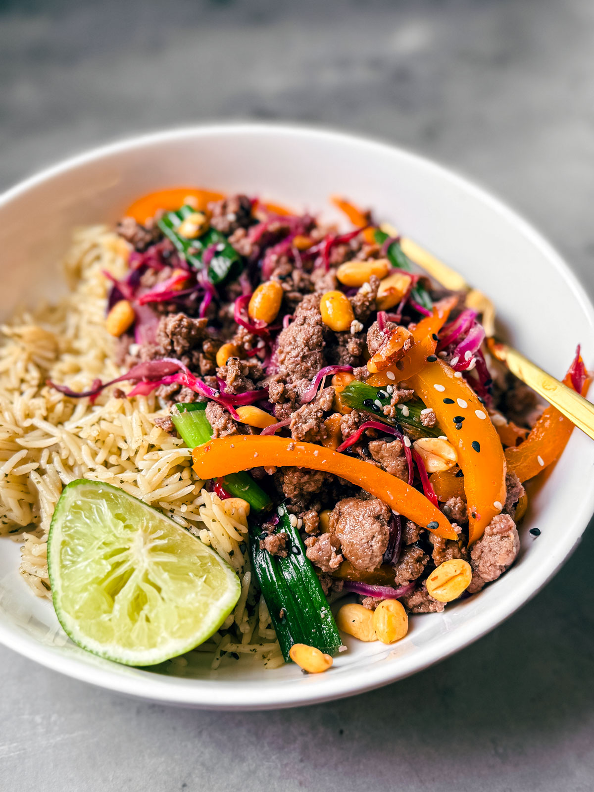 Bowl of ground beef stir fry over rice with a lime wedge.